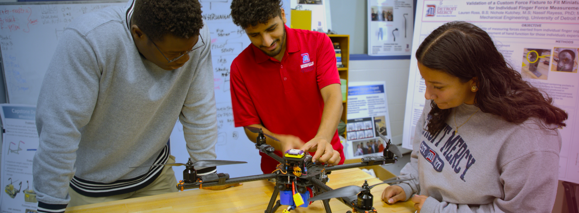 Three students, two male and one female, working on a drone.