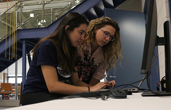 Two female students look at a computer.