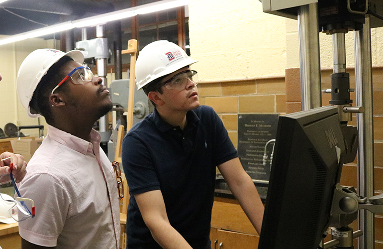 two engineering students in hard hats at a computer